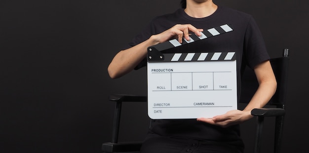 Ręka modelki trzyma białą tablicę z klapkami lub tabliczkę filmową do wykorzystania w produkcji wideo i przemyśle filmowym na czarnym tle.