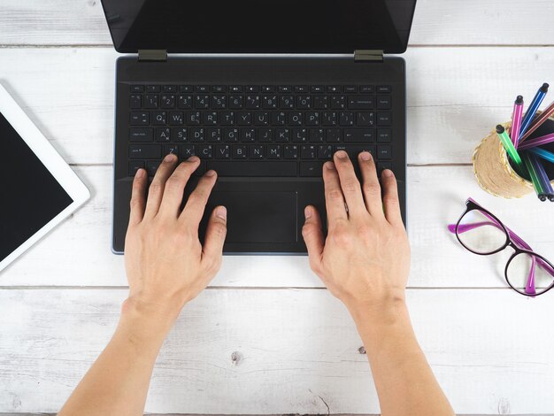 Ręka na klawiaturze laptopa z okularami i telefonem komórkowym na widoku z góry stołu