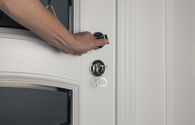 Ręka otwiera drzwi za pomocą metalowej klamki i klucza w zamku drzwi z kluczem w kształcie zbliżenia domu Koncepcja nieruchomości i zakup mieszkania