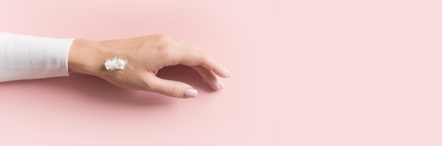 Zdjęcie ręka pięknej młodej dziewczyny z kremem na różowym pastelowym tle koncepcja szablon kobiecy blog media społecznościowe koncepcja piękna baner internetowy