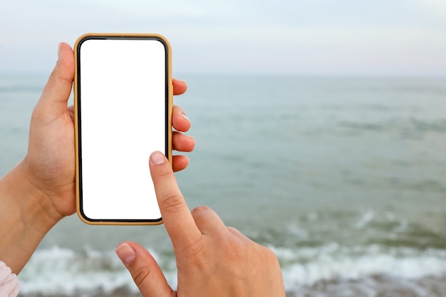 Ręka Pokazująca Pusty Inteligentny Telefon Na Plaży Z Morzem W Tle. Makieta Białego Ekranu