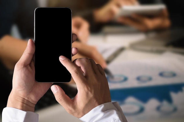Ręka trzyma biały telefon komórkowy z pustym białym ekranem w biurze.