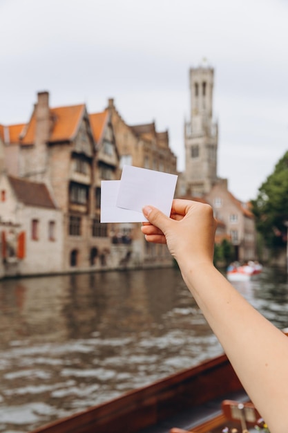 Ręka trzyma bilet lub wizytówkę z miejscem na kopię na tle kanału i średniowiecznych domów w Brugii w Belgii