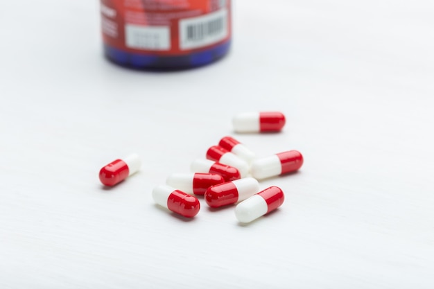 Ręka trzyma czerwone i białe tabletki na białym tle tabeli. Koncepcja leków witamin i mikroelementów. Leczenie i zapobieganie.