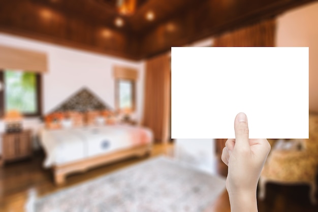 Ręka trzyma czysty papier z rozmytym tłem wnętrza domu