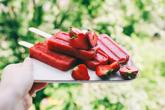 Ręka trzyma domowe lody Truskawkowe Popsicles