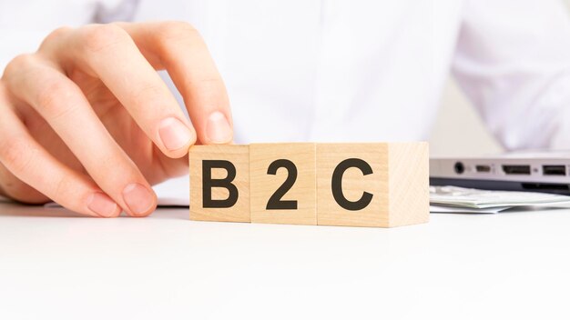 Ręka trzyma drewnianą kostkę z tekstem B2C na tle tabeli koncepcji marketingu finansowego i biznesu