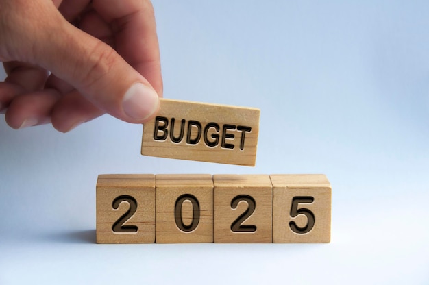 Ręka trzyma drewniany klocek z tekstem Budżet 2025 z niewyraźnym tłem przyrody Koncepcja rocznego budżetu