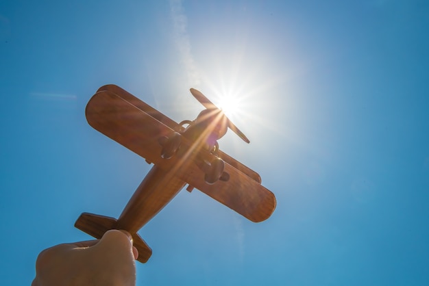 Ręka trzyma drewniany samolot na tle słońca