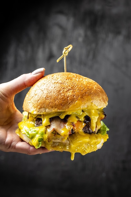 Ręka trzyma duży apetyczny ugryziony burger na ciemnym betonowym tle koncepcja fast foodów i fast foodów pionowe miejsce obrazu dla tekstu