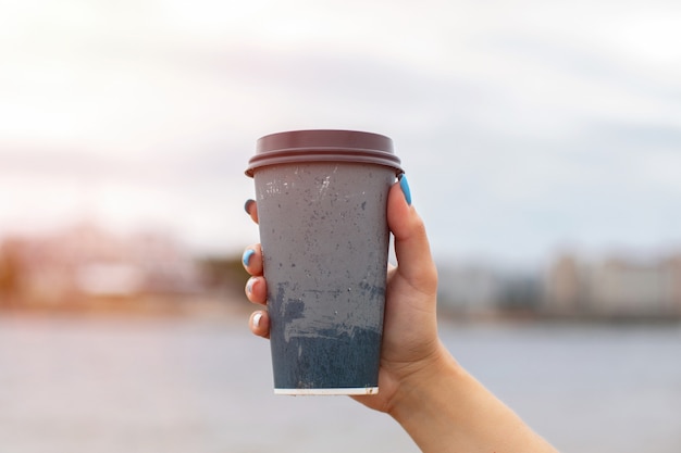 Ręka trzyma filiżankę kawy na tle morza w czasie zachodu słońca