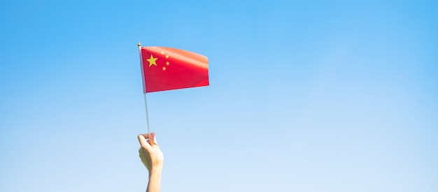 Zdjęcie ręka trzyma flagę chin na tle błękitnego nieba. święto narodowe chińskiej republiki ludowej, dzień świąt państwowych i koncepcje szczęśliwego świętowania