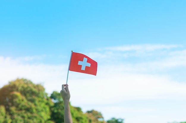 Ręka trzyma flagę Szwajcarii na tle błękitnego nieba. Koncepcje Święta Narodowego Szwajcarii i szczęśliwego święta