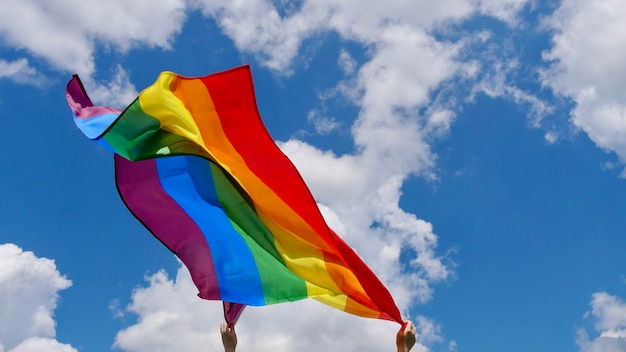 Ręka trzyma flagę tożsamości płci LGBT na tle niebieskiego pochmurnego nieba w słoneczny wietrzny letni dzień podczas obchodów miesiąca godności na paradzie