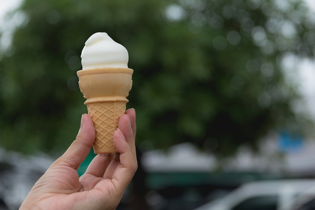 Ręka trzyma miękki biały dojnej śmietanki lody rożek w letnim dniu na natury tle.