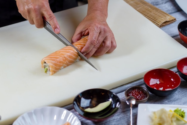 Ręka trzyma nóż tnie sushi. Gruba rolka sushi. Szef kuchni sushi gotuje obiad. Sprawdzona receptura kuchni japońskiej.