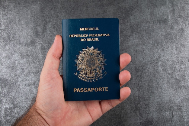 Ręka trzyma paszport brazylijski z szarym tłem