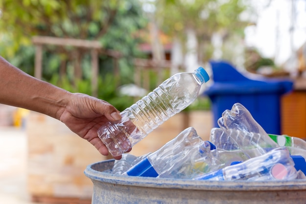 Ręka trzyma plastikową butelkę do recyklingu w koszu na śmieci do czyszczenia.