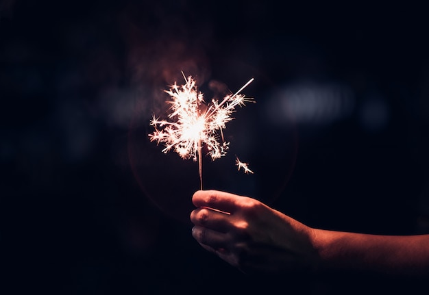 Ręka trzyma płonącego sparkler wybuch na czarnym tle