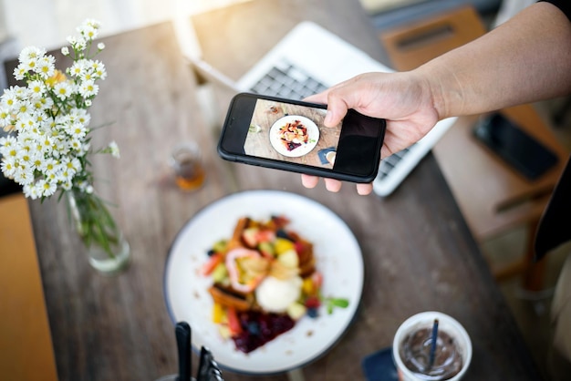 Ręka trzyma smartfon biorąc francuskie tosty polewają mieszane lody owocowe włoskie napoje gazowane na drewnianym stole w nowoczesnej jasnej kuchni wnętrza