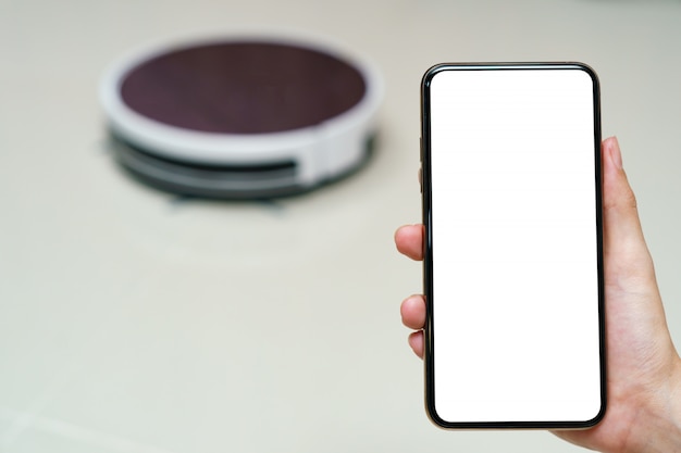 Zdjęcie ręka trzyma smartfon z ekranem wygaszającym do sterowania robotem odkurzacza