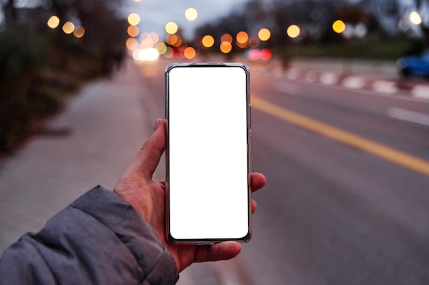 Zdjęcie ręka trzyma smartphone z pustego ekranu z kopią miejsca na projekt lub logo makieta telefonu komórkowego wieczorem ulicy miasta na tle światła bokeh