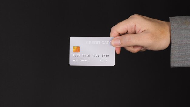Zdjęcie ręka trzyma srebrną kartę kredytową na czarnym tle