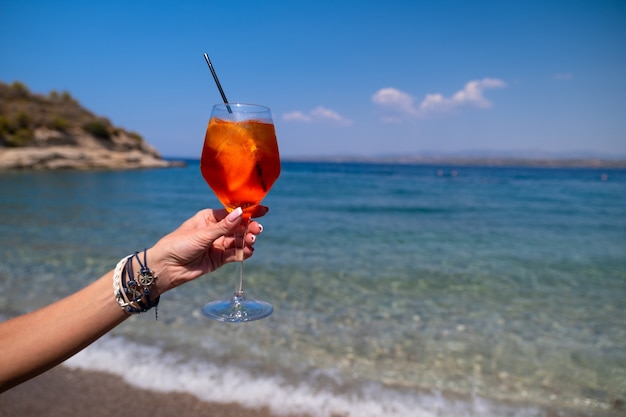 Ręka trzyma szklankę koktajlu aperol spritz na tle morza