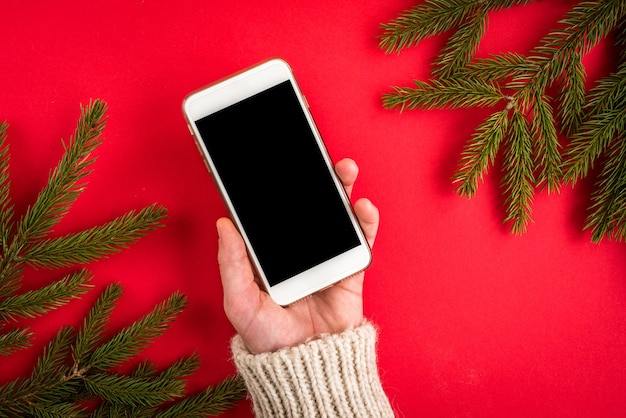 Ręka trzyma telefon komórkowy na czerwono z gałęzi jodły Boże Narodzenie.