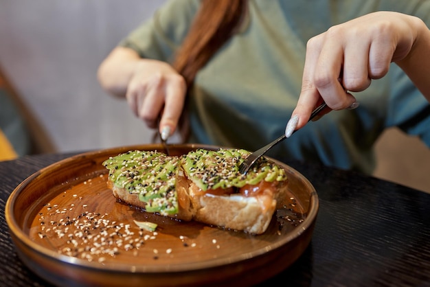 Ręka trzyma zdrowe tosty z awokado dojrzałe hass awokado pełnoziarnisty chleb sezamowy nasiona lnu wegańskie