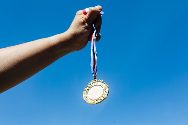 Zdjęcie ręka trzyma złoty medal za pierwsze miejsce na tle nieba. koncepcja zwycięstwa