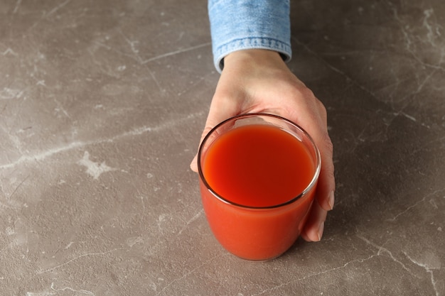 Ręka trzymać szklankę soku pomidorowego na szaro