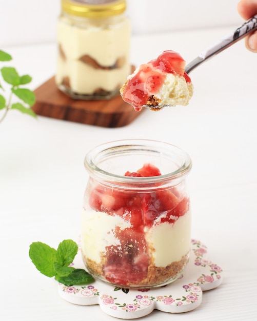 Ręka trzymaj łyżkę z tradycyjnym włoskim deserem Panna Cotta truskawkowym waniliowym w słoikach Vintage ze świeżymi jagodami na białym tle drewnianych.