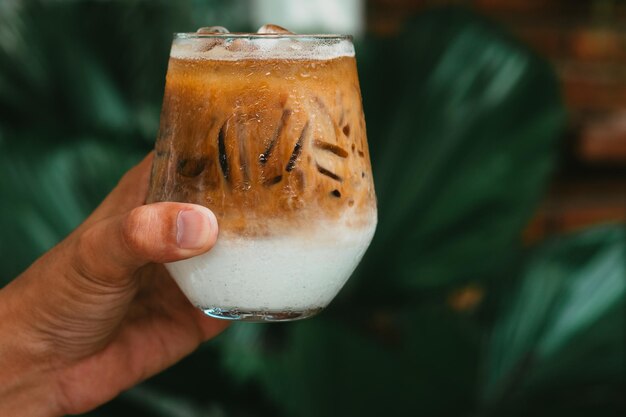 Ręka trzymaj mrożoną kawę latte w szklance ze śmietaną na dole zimnego letniego napoju w tle