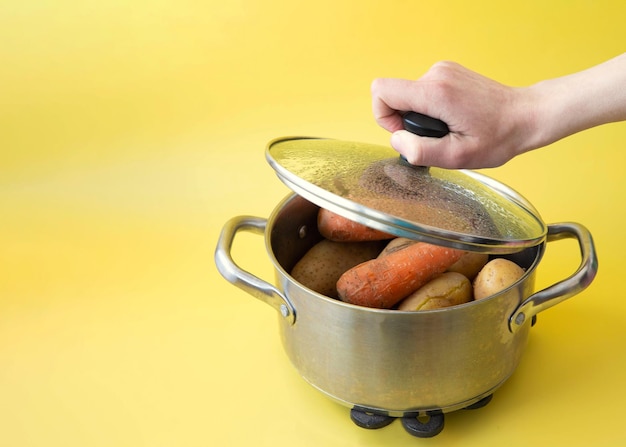Ręka Unosi Pokrywkę Z Garnka Z Gotowanymi Warzywami Na żółtym Tle