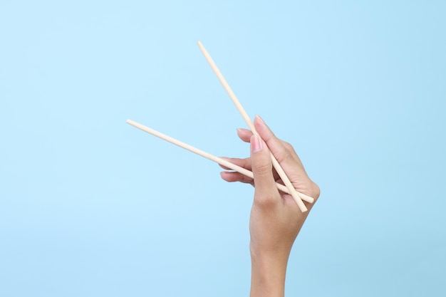 Zdjęcie ręka używająca bambusowych pałeczek na niebieskim tle