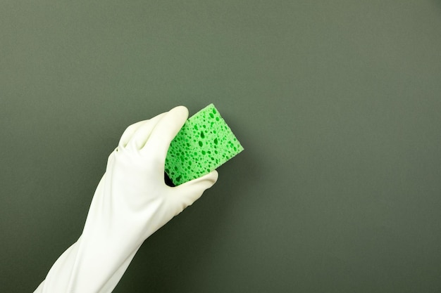 Ręka w gumowej rękawiczce trzyma gąbkę do mycia na zielonym tle