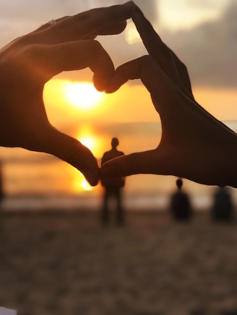 Zdjęcie ręka w kształcie serca na plaży podczas zachodu słońca