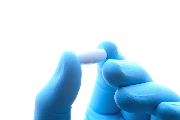 Zdjęcie ręka w niebieskiej rękawiczce medycznej trzyma zbliżenie białej pigułki