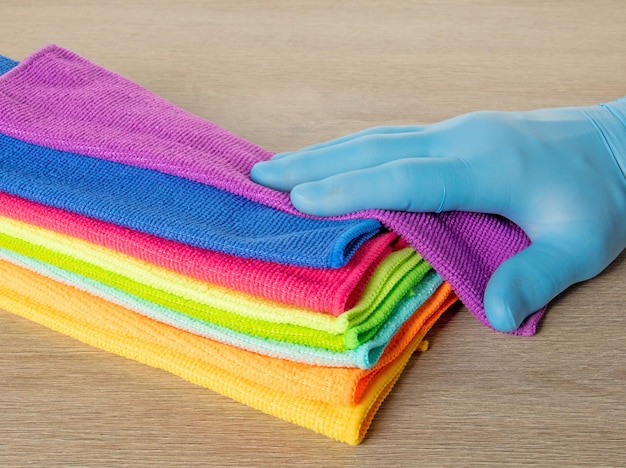 Ręka w niebieskiej rękawiczce wybiera ręcznik ze stosu jasnych ręczników z mikrofibry do czyszczenia