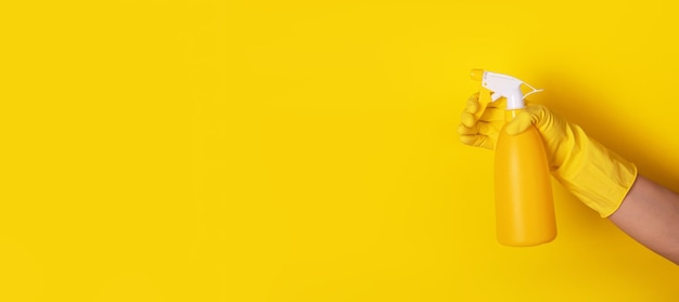 Ręka w rękawiczce trzymająca butelkę z rozpylaczem na żółtym tle, koncepcja czystości, panoramiczny układ