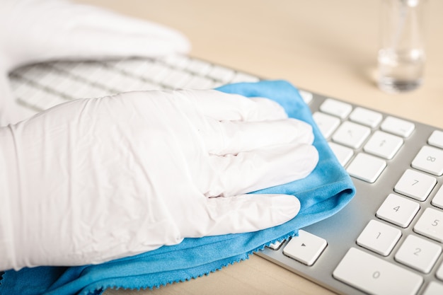 Ręka w rękawiczkach do czyszczenia klawiatury środkiem dezynfekującym. COVID-19 Koncepcja zapobiegania zanieczyszczeniom wywołanym przez epidemię koronawirusa