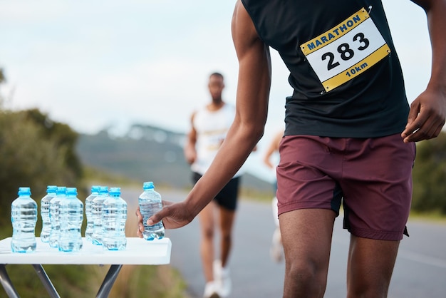 Ręka w wodzie i biegacz maratonu w wyścigu lub konkursie zbliżenie do fitnessu lub cardio na ulicy Ćwiczenia sportowe lub bieganie z sportowcem chwytającym drinka na zewnątrz na drodze do treningu