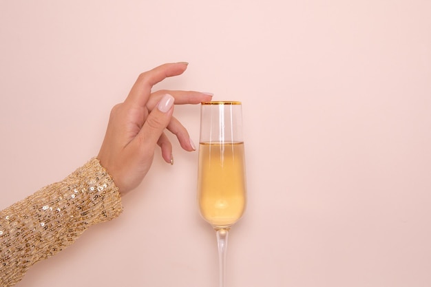 Ręka w złotej sukience trzymająca kieliszek szampana na beżowym tle