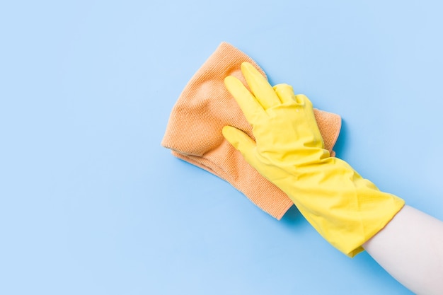 Ręka w żółtej gumowej rękawiczce myje ścianę pomarańczową miękką szmatką, czyszcząc i myjąc ściany