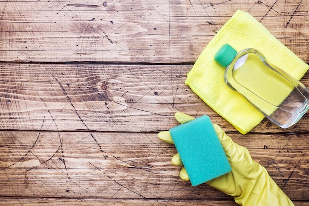 Ręka w żółtej rękawiczce i cleaning gąbce dla czyścić na drewnianym tle.