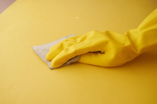 Ręka w żółtych gumowych rękawiczkach do czyszczenia stołu szmatką