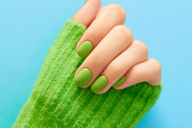 Ręka Womans z zielonym manicure bliska na niebieskim tle Pielęgnacja ciała spa Zabiegi kosmetyczne Koncepcja salonu
