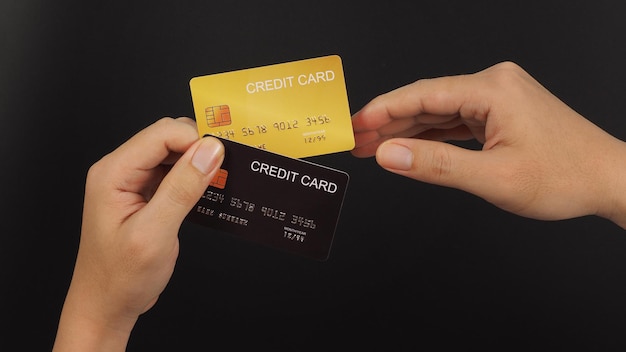 Zdjęcie ręka wybiera dwie karty kredytowe w kolorze czarnym i złotym na czarnym tle