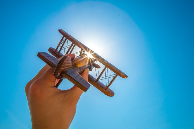 Ręka wystrzeliwuje drewniany samolot na tle słońca